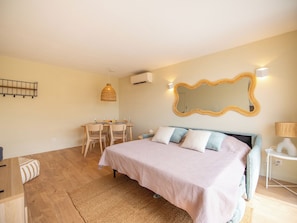 Ein Schlafzimmer mit Bett, Nachttisch, Lampe sowie einem Essbereich mit Stühlen und Tisch.