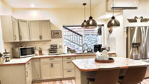 A kitchen with a central island, bar stools, a microwave, a toaster, and pendant lights. - Lux Lodge Downtown w/ AC, Bonus Cottage, Courtyard (McCall)
