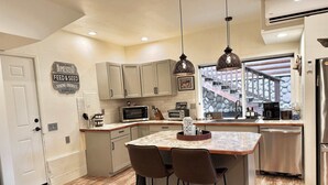 A kitchen with a central island, bar stools, a microwave, toaster, and a coffee maker. - Lux Lodge Downtown w/ AC, Bonus Cottage, Courtyard (McCall)