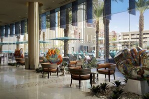 A hotel lobby with large windows, palm trees, and colorful abstract sculptures.