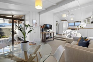 Ein modernes Wohnzimmer mit einem Glastisch, weißen Sofas, einem Fernseher und einem Balkon mit Gartenmöbeln.
