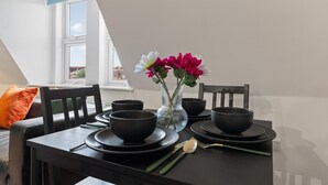 A dining table set with black bowls and plates, a vase with flowers, and a window with a view of buildings. - Luxury Apartment Near Football Stadium Nottingham (West Bridgford)
