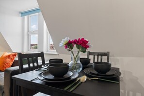 A dining table set with black bowls and plates, a vase with flowers, and a window with a view of buildings. - Luxury Apartment Near Football Stadium Nottingham (West Bridgford)