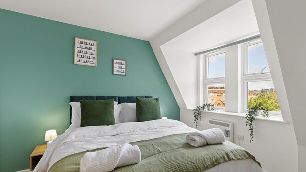 A bedroom with a bed, a nightstand, a window with a view, and two wall-mounted signs. - Luxury Apartment Near Football Stadium Nottingham (West Bridgford)
