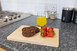 A kitchen counter with a cutting board holding cookies and strawberries, a glass of yellow liquid, and kitchen appliances. - Luxury Apartment Near Football Stadium Nottingham (West Bridgford)