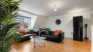 A modern living room with a black leather sofa, a glass coffee table, and a black refrigerator. - Luxury Apartment Near Football Stadium Nottingham (West Bridgford)