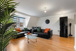 A modern living room with a black leather sofa, a glass coffee table, and a black refrigerator. - Luxury Apartment Near Football Stadium Nottingham (West Bridgford)