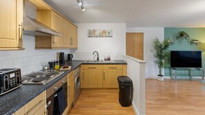 A modern kitchen with wooden cabinets, a built-in oven, a sink, and a countertop with various appliances. - Luxury Apartment Near Football Stadium Nottingham (West Bridgford)