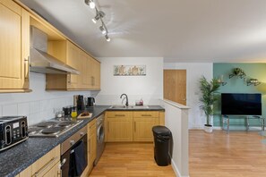 A modern kitchen with wooden cabinets, a built-in oven, a sink, and a countertop with various appliances. - Luxury Apartment Near Football Stadium Nottingham (West Bridgford)