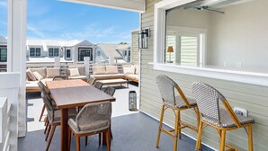 Eine überdachte Terrasse mit Esstisch und Stühlen, einem Deckenventilator und Blick auf benachbarte Häuser.