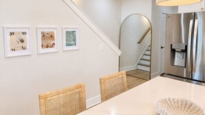 Eine moderne Küche mit einem Edelstahl-Kühlschrank, eine Essecke mit einem weißen Tisch und Korbstühlen sowie eine Treppe mit weißer Geländer.