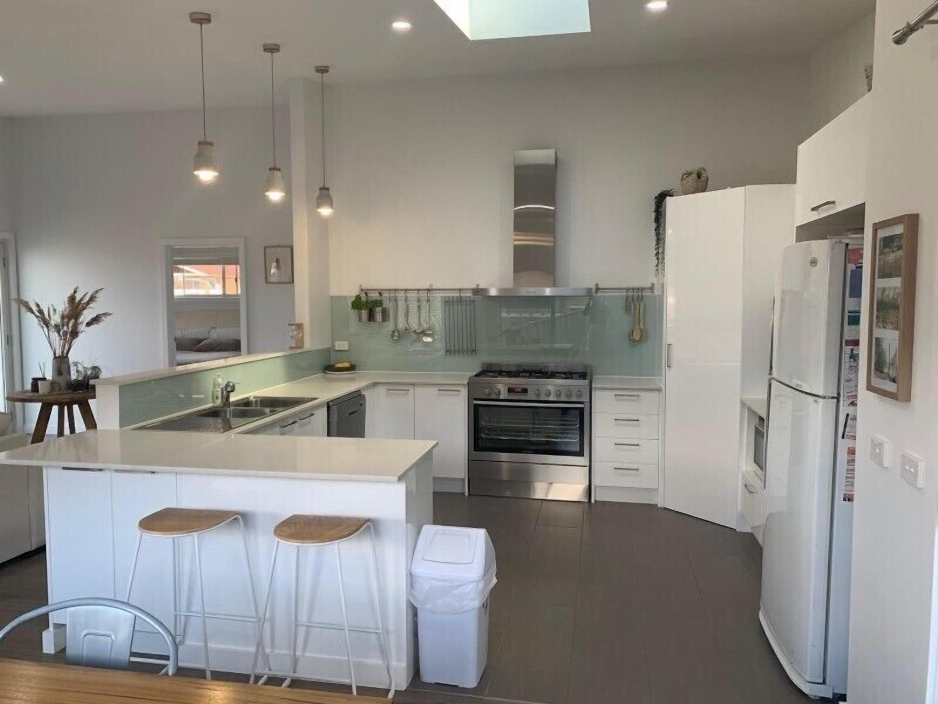 A modern kitchen with a central island, bar stools, a built-in oven, and white cabinetry.