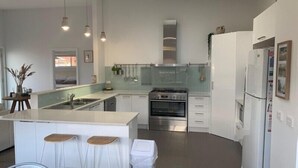 Une cuisine moderne dotée d’un îlot central, de tabourets de bar, d’un four encastré et de meubles de rangement blancs.