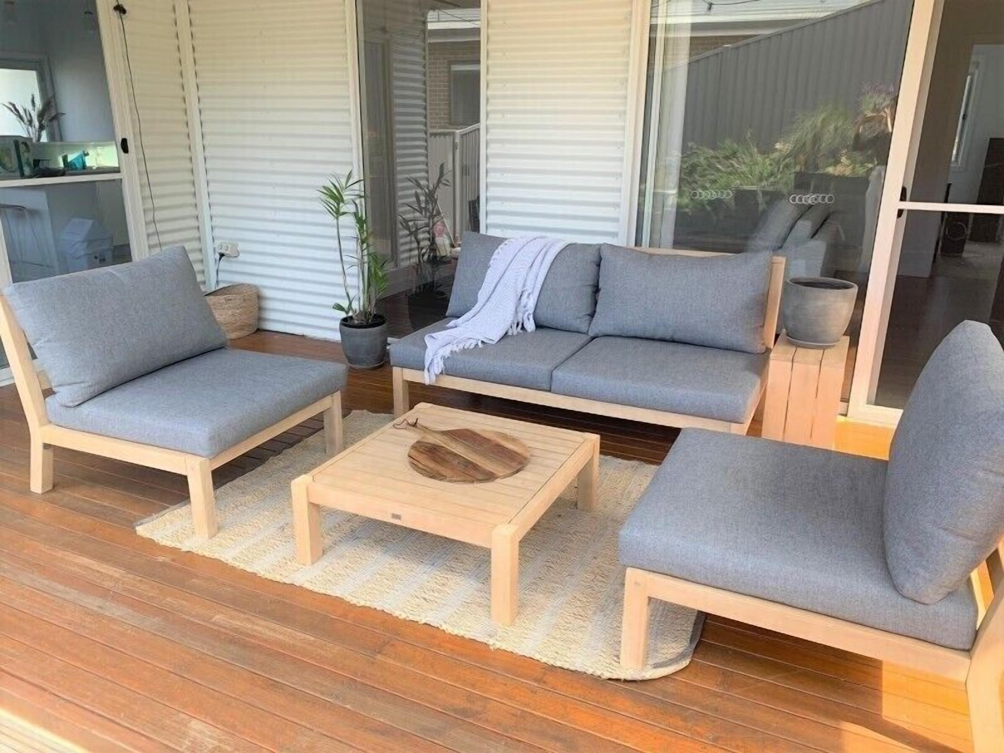 A modern outdoor seating area with a sofa, two armchairs, and a wooden coffee table.