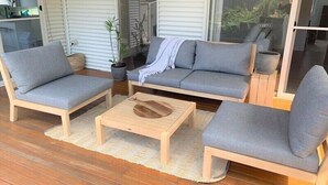 Un espace extérieur moderne aménagé avec un canapé, deux fauteuils et une table basse en bois.