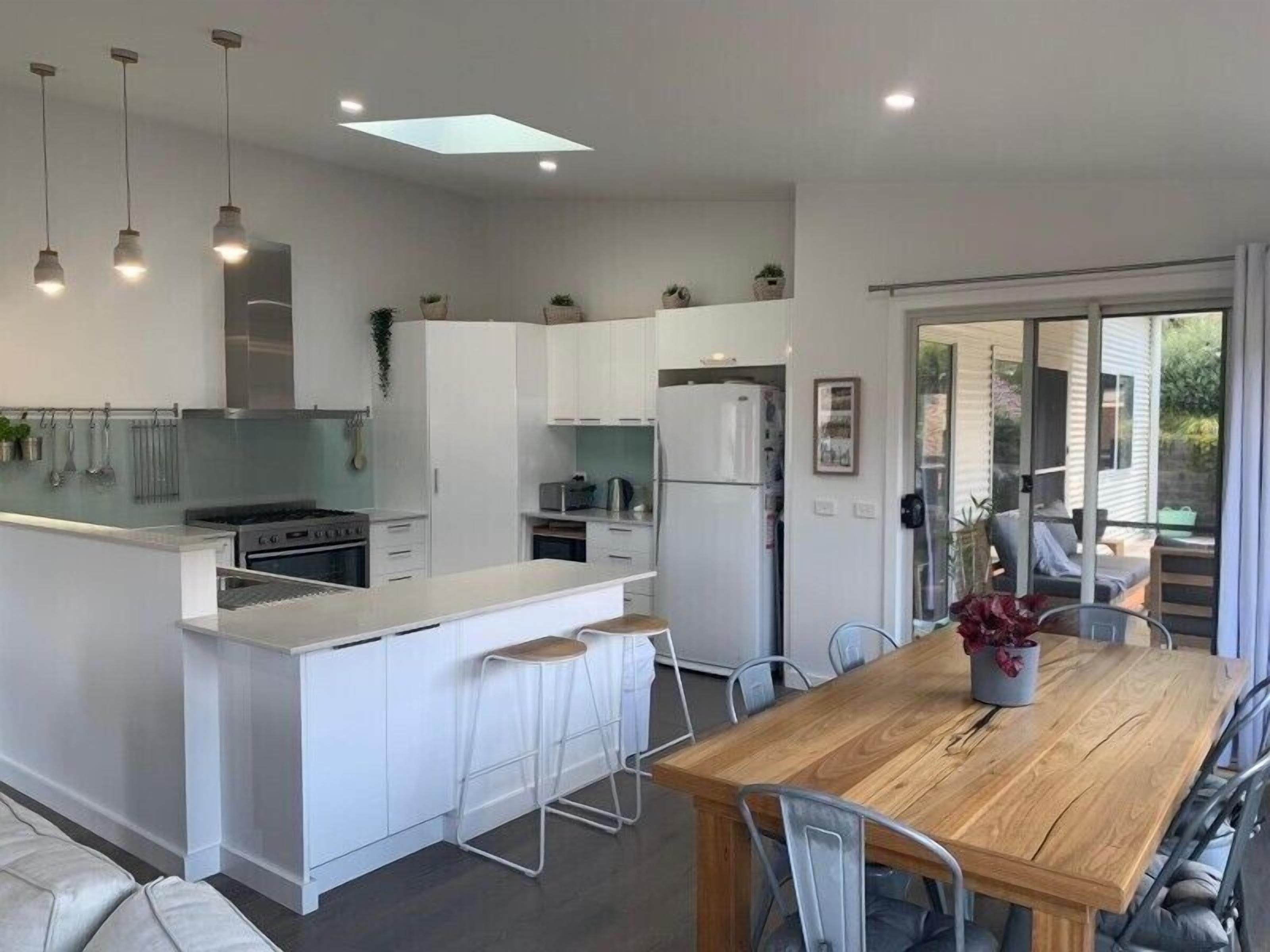 A modern kitchen with white cabinetry, a wooden dining table, and a bar area.