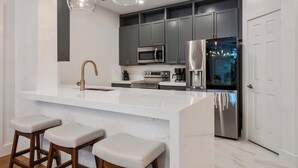 Una cocina moderna con una isla grande, electrodomésticos de acero inoxidable y taburetes de bar.