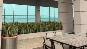 A rooftop patio with a table and chairs, large windows overlooking the sea, and a potted plant.
