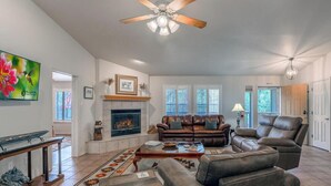 A living room with a fireplace, leather sofas, a coffee table, and a ceiling fan. - Lazy D Cabin: Inspired by a West Texas ranch. Built for mountain memories. (Ruidoso)