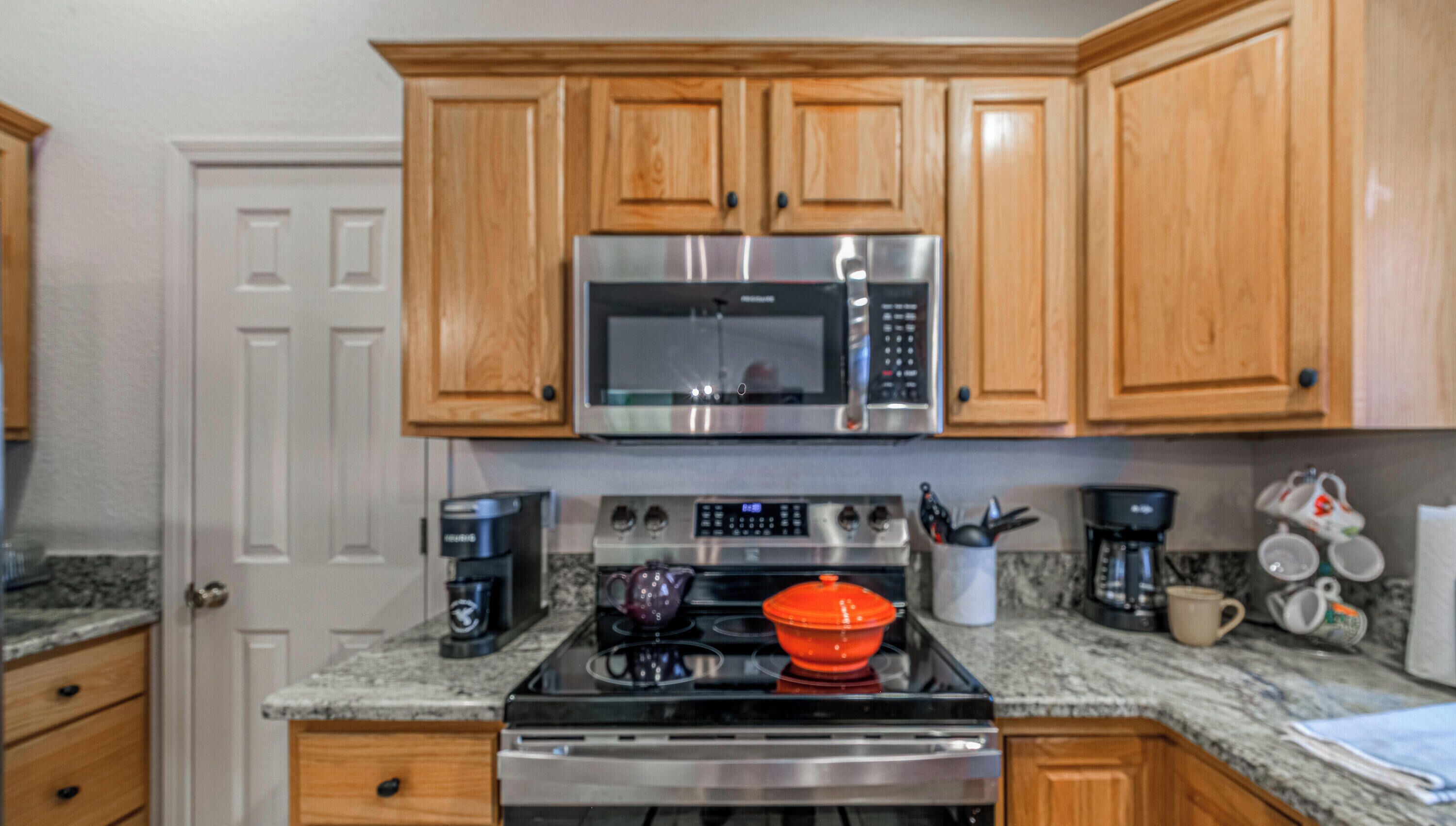A kitchen with wooden cabinets, a stainless steel microwave, a coffee maker, and a red pot on the stove.