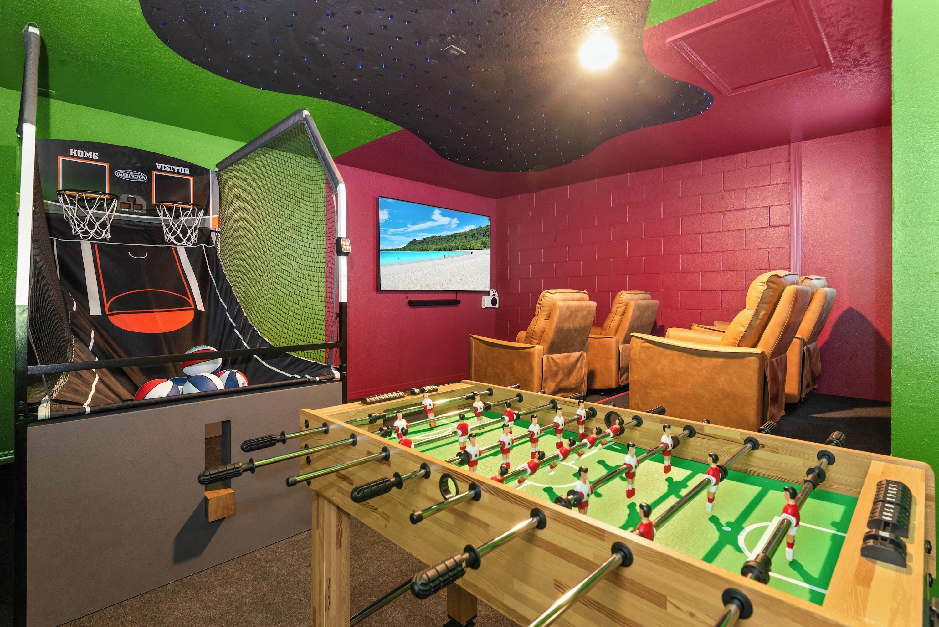 A room with a foosball table, a basketball arcade, and a TV screen displaying a beach scene.