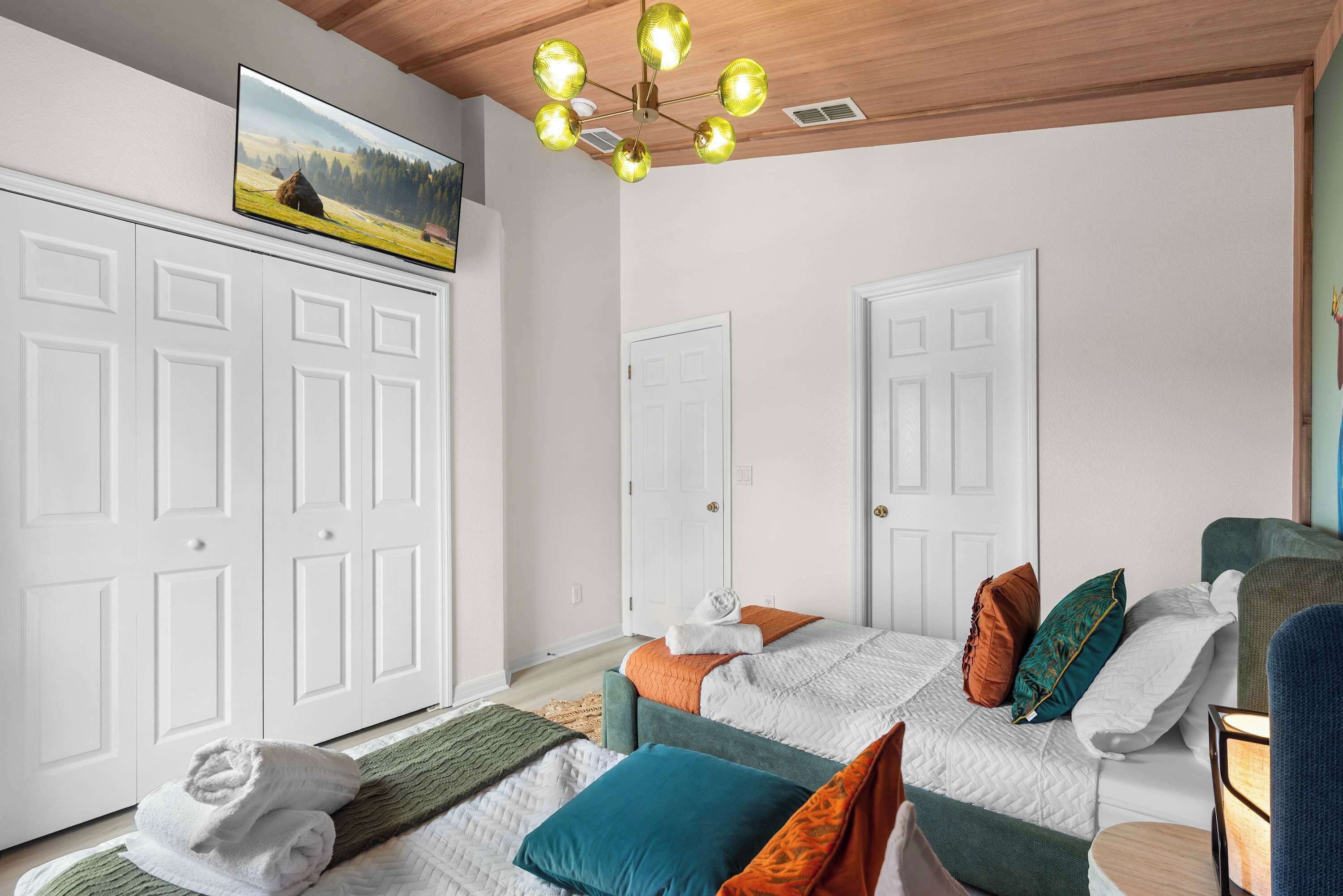 A bedroom with a bed, a TV, a chandelier, and white doors.