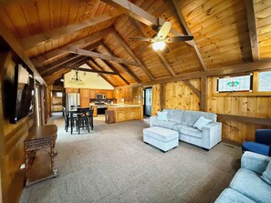 Ein geräumiger Loft mit hohen Decken, Holzbalken, einer Küchenzeile, einem Esstisch und einer Sitzecke mit Sofa und Hocker.