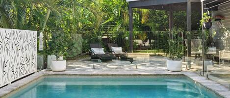 Ein Schwimmbecken mit Liegestühlen, umgeben von üppiger Vegetation und einer Pergola.