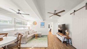 Ein modernes Wohnzimmer mit einer Couch, einem Esstisch, Stühlen, Deckenventilatoren und einem Fernseher.