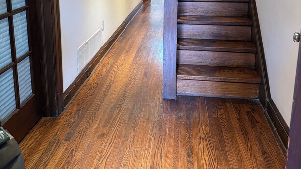 Una escalera de madera con barandilla, un pasillo con piso de madera y una puerta con ventanal.