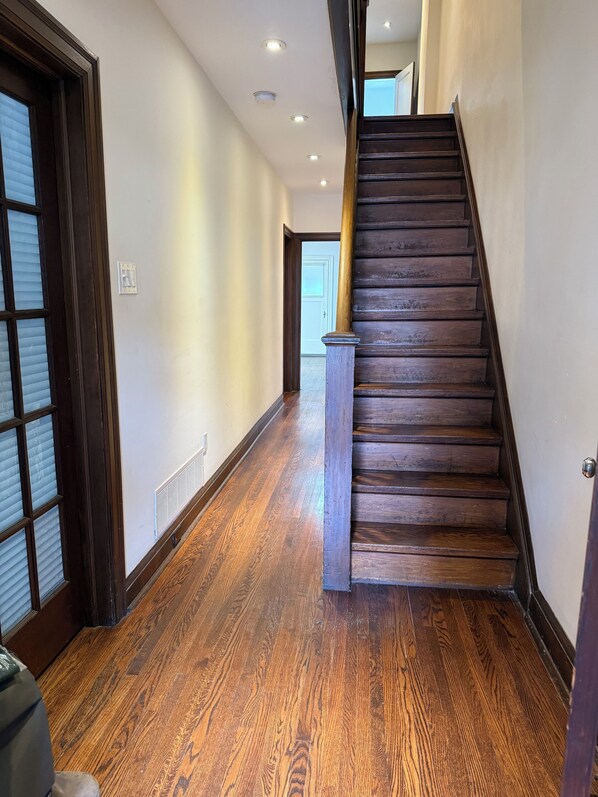 Un escalier en bois avec une rampe, un couloir au plancher de bois et une porte avec une fenêtre.