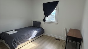 Un dormitorio con cama, ventana con cortina, escritorio y silla.