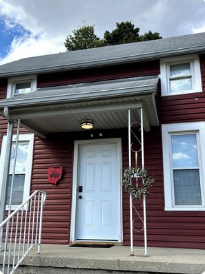 A two-story building with a white door, a red 'Ohio' sign, and a small porch with a railing. - Welcome to Red and Ready! Pet Friendly. AC's in both bedrooms for comfort. (Springfield)