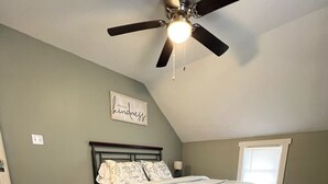Une chambre à coucher avec un lit, un ventilateur de plafond, une fenêtre et un mur sur lequel est accroché un panneau.