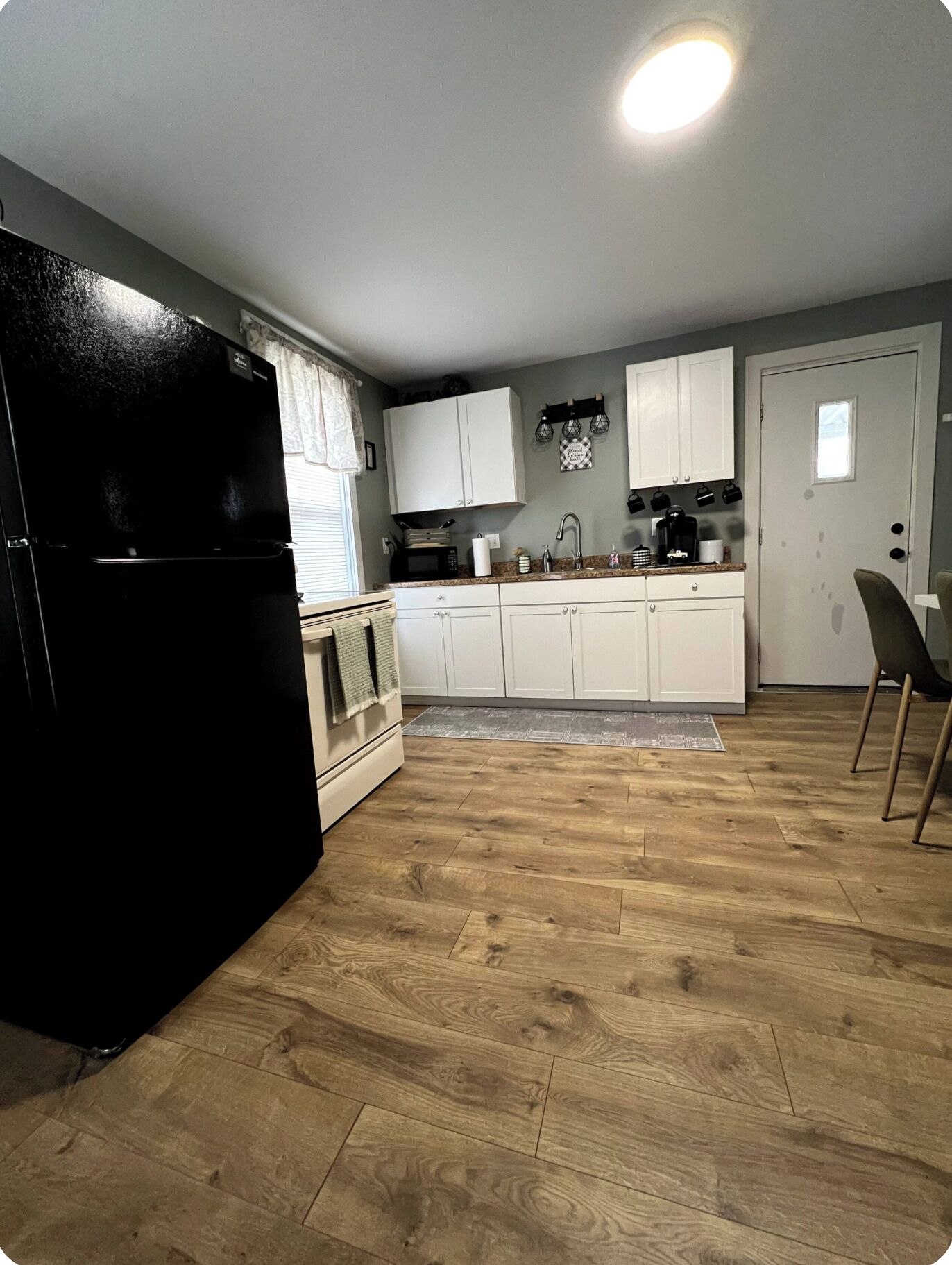 A kitchen with white cabinets, a black refrigerator, and a wooden floor.