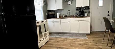 A kitchen with white cabinets, a black refrigerator, and a wooden floor.