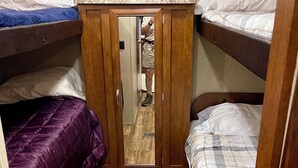 Ein schmales Zimmer mit Etagenbetten, einem Holzschrank und einem Spiegel.
