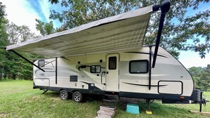 Ein Wohnmobil mit überdachten Wohnbereich, einer Schiebetür und einer kleinen Stufe zum Eingang.