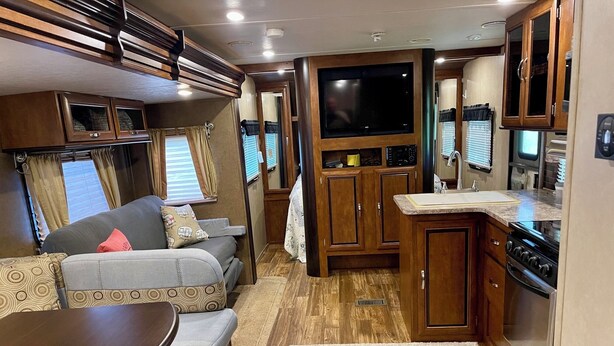 Ein kompaktes Wohnmobil-Interieur mit einer Küchenzeile, einer Sitzecke mit Tisch und einem Fernseher, der über den Schränken angebracht ist.