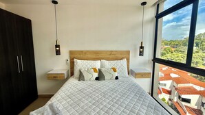 Een slaapkamer met een groot bed, twee nachtkastjes, een kledingkast en uitzicht op gebouwen door een raam.