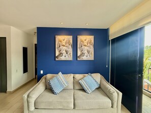 Ein Zimmer mit einem beigen Sofa, zwei abstrakten Gemälden und einem großen Fenster.