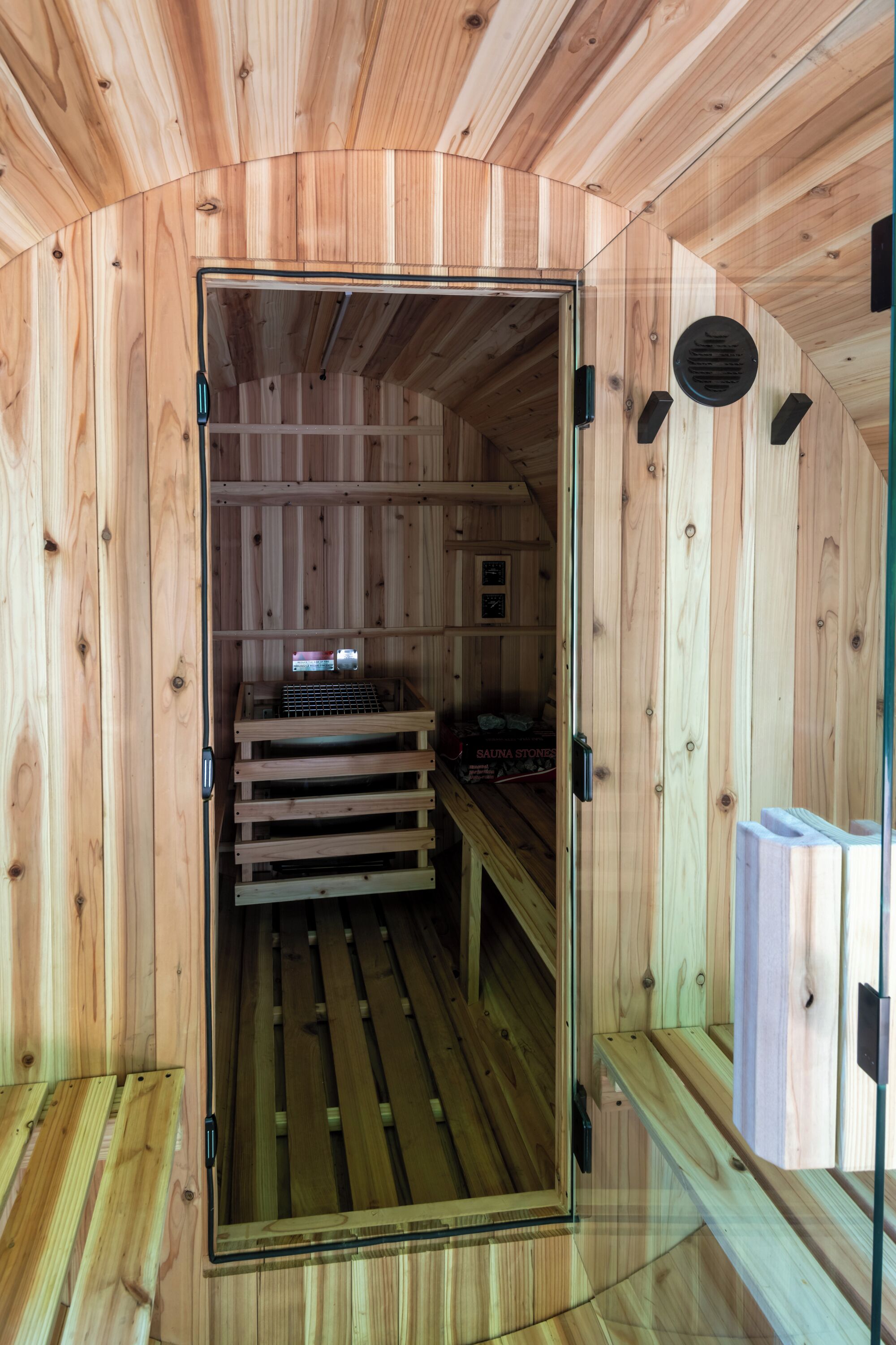 Una sauna con paredes y bancos de madera, una puerta de cristal y un pequeño estante con objetos.