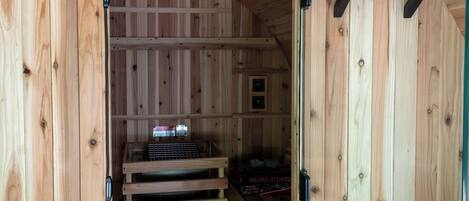 Una sauna con paredes y bancos de madera, una puerta de cristal y un pequeño estante con objetos.