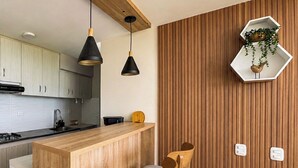 Une cuisine moderne avec des meubles en bois, un îlot central, deux tabourets de bar, un éclairage suspendu et un lambris en bois.