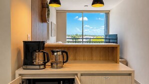 Une cuisine compacte équipée d’un four à micro-ondes encastré, d’une machine à café et d’une bouilloire, d’un plan de travail en bois et d’un éclairage suspendu.