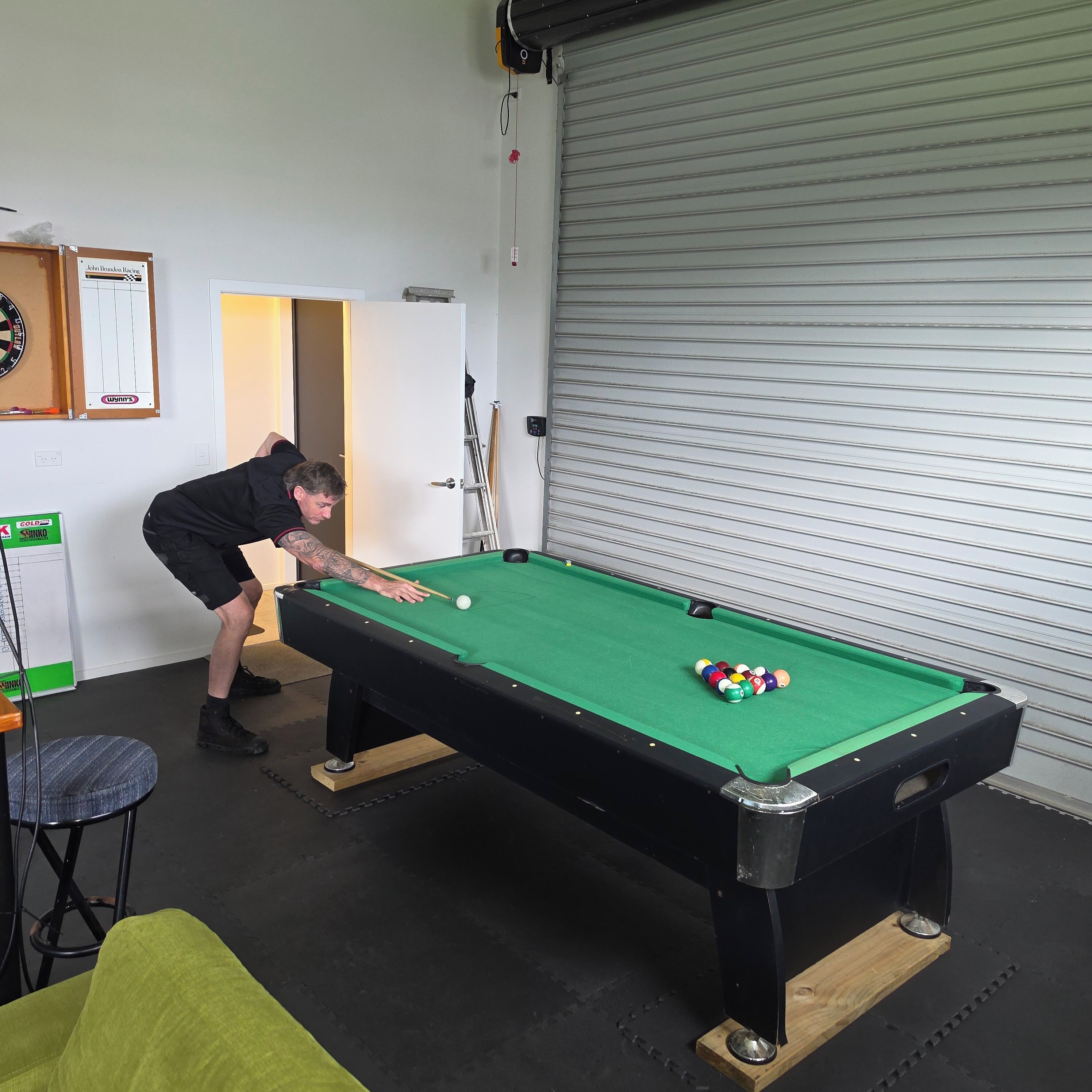 A pool table with a person playing, a dartboard, and a closed garage door.