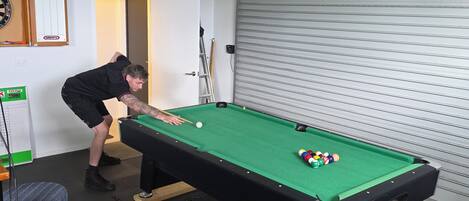 A pool table with a person playing, a dartboard, and a closed garage door.