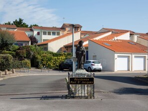 Une rue résidentielle bordée d’une statue, de voitures garées et de maisons aux toits recouverts de tuiles rouges.