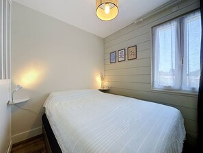 Une chambre à coucher avec un lit, des lampes de chevet, une fenêtre avec des rideaux et des tableaux accrochés au mur.