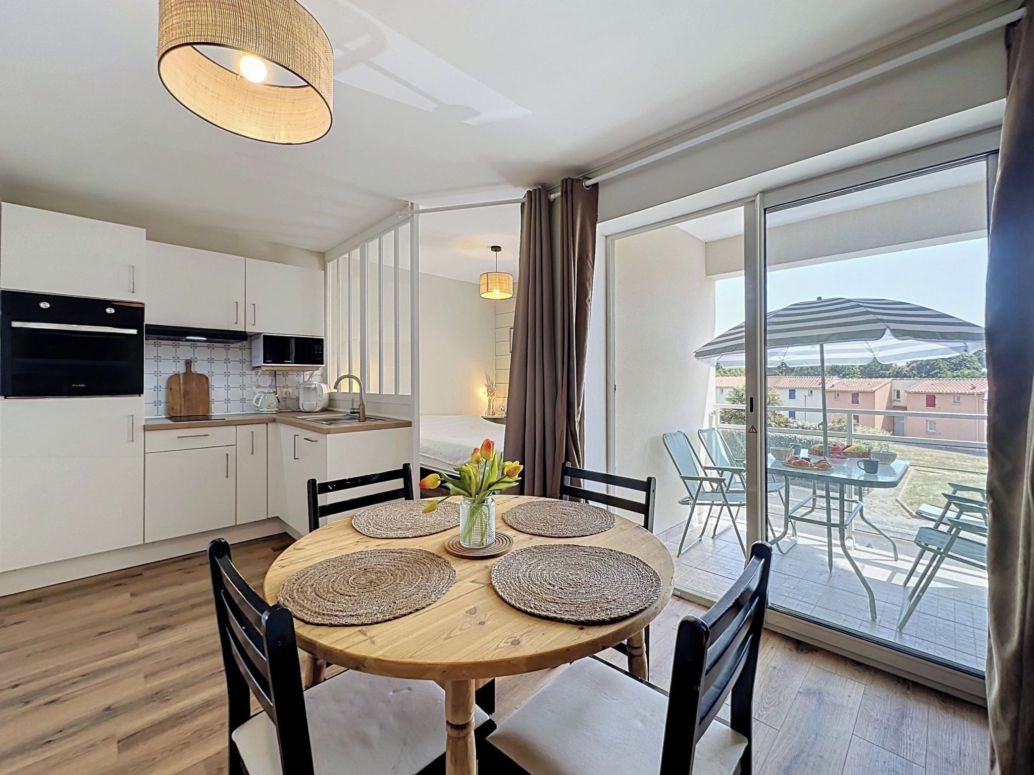 A modern kitchen with a dining area, large sliding glass doors to a balcony, and a view of the neighborhood.